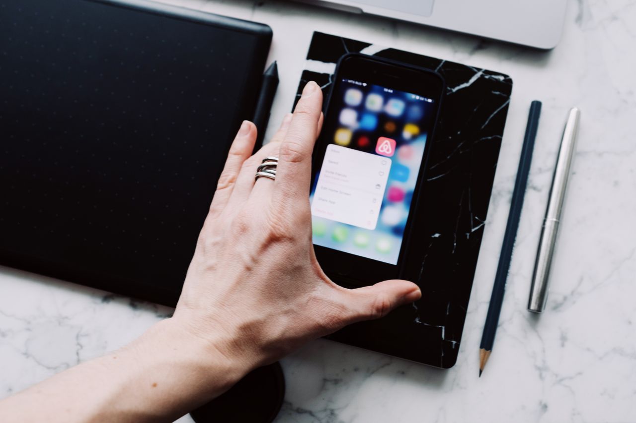Vue d’en haut d’une personne sans visage consultant un téléphone mobile tout en travaillant à la maison sur une table en marbre blanc, avec des gadgets, un stylo et un crayon